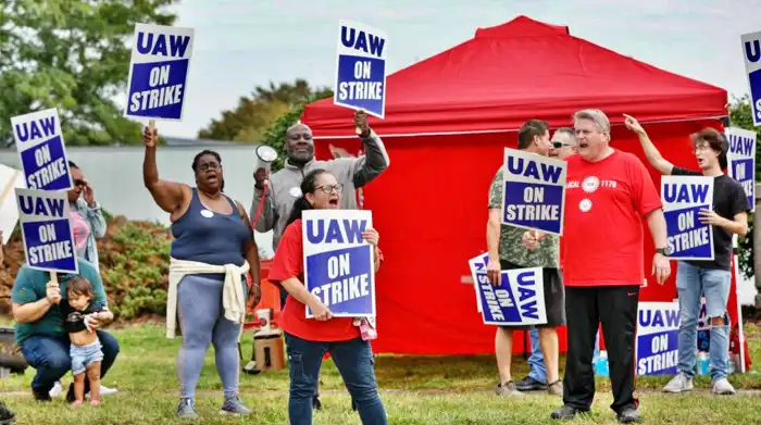 Miembros de UAW y trabajadores de la línea Mopar Parts Center en Center Line, Michigan, sostienen carteles fuera de las instalaciones después de abandonar sus trabajos al mediodía del 22 de septiembre de 2023. (Foto de KAMIL KRZACZYNSKI / AFP) (Foto de KAMIL KRZACZYNSKI/AFP vía Getty Images)